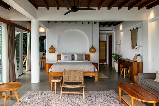 Wide bedroom with exposed beams, arched headboard, layered textures