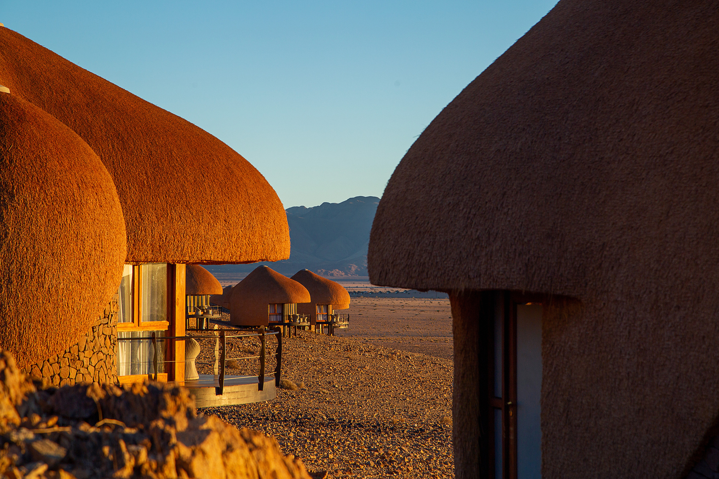 Thatched lodge dome at sunset, distant Namib mountains