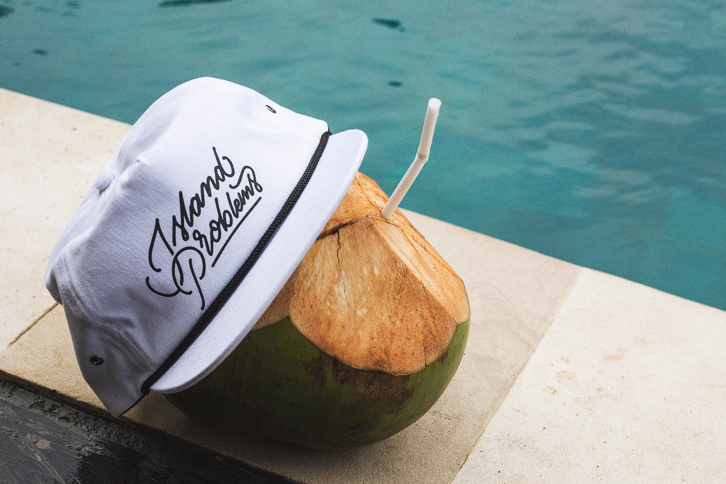 Product still life — branded cap and young coconut at poolside